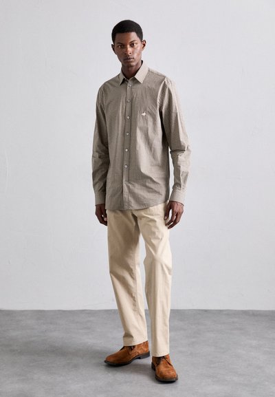 Camisa de cuadros marrón y blanco con botones, pantalones beige y zapatos de ante marrones; la camisa tiene un pequeño parche en el pecho.