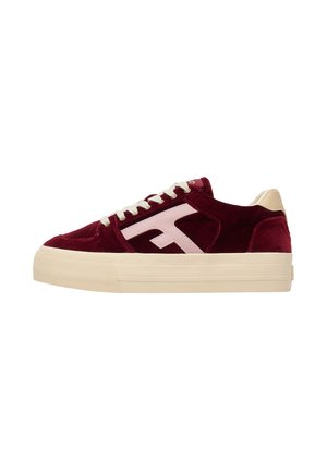 Zapatilla baja con parte superior de terciopelo burdeos, suela crema, cordones blancos y un logo estilizado en rosa pálido en el lateral.
