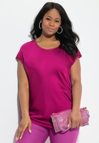 Haut fuchsia à manches courtes avec encolure ronde, associé à un pantalon assorti et une petite pochette en sequins roses. Texture lisse.
