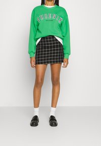 Grön sweatshirt med trycket "PHOENIX ARIZONA", matchad med en svart rutig minikjol. Svarta loafers och vita strumpor fulländar looken.