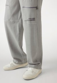 Light gray cargo pants with two zippered pockets and printed logo. Pairing with white sneakers featuring perforated detailing and a chunky sole.