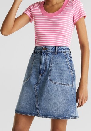Femme portant un t-shirt rayé rose et blanc à manches courtes, rentré dans une jupe en jean bleue taille haute avec des poches à l'avant.