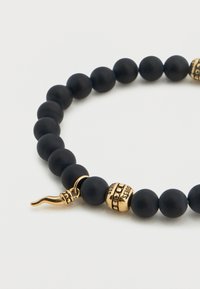 Μαύρο βραχιόλι με ματ χάντρες, διακοσμημένο με χρυσούς τόνους και διακοσμητικό κούμπωμα. Ο σχεδιασμός περιλαμβάνει διαδοχικά μεγέθη χάντρων για υφή.