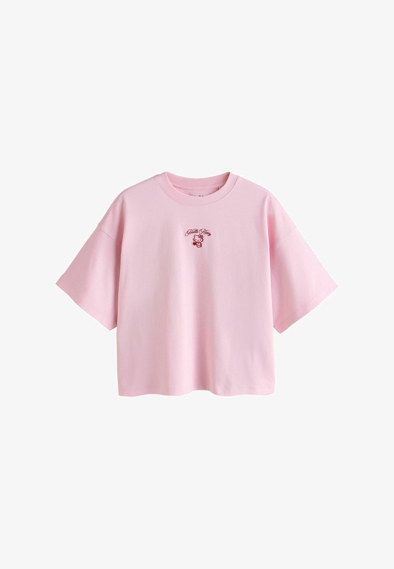 T-shirt ample à manches courtes rose pâle avec petit graphisme Hello Kitty rouge et texte centré sur la poitrine.