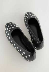 Black leather ballet flats featuring large white polka dots, rounded toe, and a smooth texture with a snug fit around the foot.