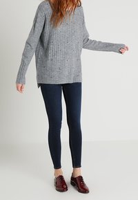 Grå rippad tröja med långa ärmar och V-ringning, i kombination med mörkblå skinny jeans och glänsande röda skor.