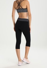 Černé capri legíny s vysokým pasem, spárované s šedou sportovní podprsenkou s křížovými popruhy na zádech a hladkým povrchem.