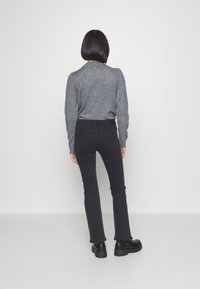 Grå tröja, svarta utsvängda jeans och svarta chunkiga stövlar. Texturen på tröjan är slät, jeansen har en klassisk denimlook med fickor.