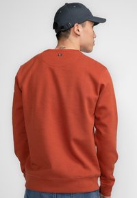 Rode sweatshirt met een ronde hals, lange mouwen en geribbelde manchetten. Heeft een eenvoudig ontwerp zonder zichtbare patronen of hardware.
