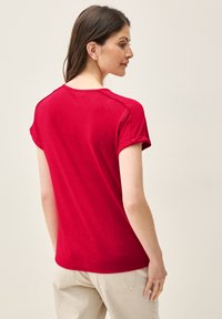 Camiseta roja de manga corta con un corte relajado, textura suave, escote redondeado y puños enrollados, combinada con pantalones beige claros.