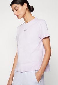 Lilac kokvilnas T-krekls ar īsām piedurknēm, citas formas kakla izgriezumu un smalku DKNY logotipu izšuvumā uz krūtīm. Patīkama tekstūra, brīvs piegriezums.