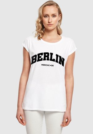 Hvit kortermet t-skjorte med fet svart tekst som leser "BERLIN MERCH•DE" i et buet design over fronten.