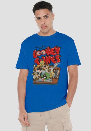 Young man wearing blue T-shirt with red "Looney Tunes" text and cartoon characters inside a vintage television set.