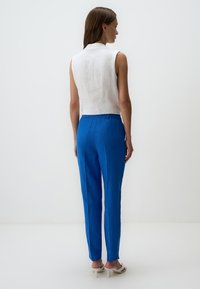 Witte mouwloze shirt met een hoge kraag, gecombineerd met blauwe linnen broek. De broek heeft een elastische tailleband en een rechte pijp.