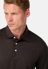 Brūns polo krekls, kas izgatavots no gludas auduma, ar apkakli un trim pogu rindām, ar pieguļošu dizainu un bez redzamām rakstzīmēm.