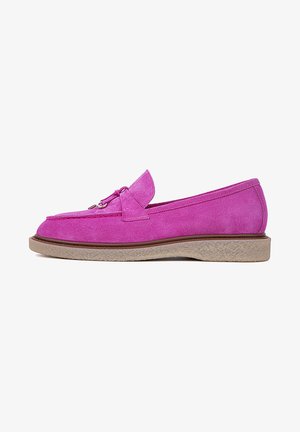 Mocassins en suede rose avec une texture douce, dotés d'un accent métalleux décoratif et d'une semelle en caoutchouc brun clair, posés sur une chaise bleue.