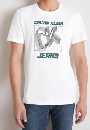 T-shirt en coton blanc avec un design graphique linéaire en noir et vert, le texte indique "CALVIN KLEIN" et "JEANS", col rond, manches courtes.