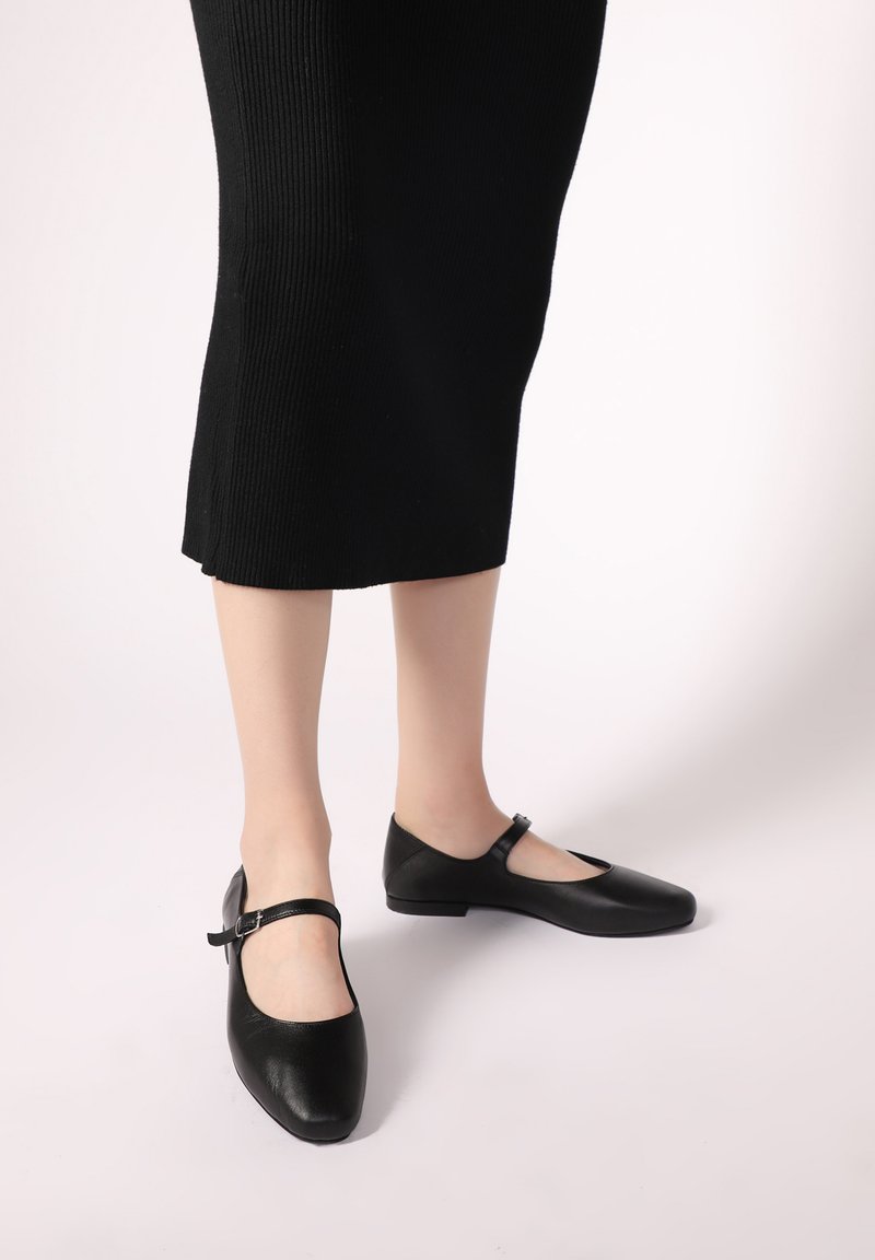 Černé kožené baleríny s kulatou špičkou, tenkým páskem přes nárt a nízkým podpatkem, kombinované s černou žebrovanou sukní.