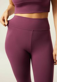 Vysoké fialové legíny vyrobené z elastického materiálu, s hladkým povrchem a minimalizovanými švy pro štíhlý vzhled.