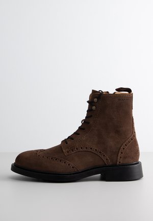 Brown suede ankle boots with a lace-up design, brogue detailing, and a black rubber sole. Features a side zipper for easy wear.