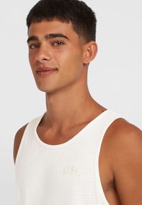 Witte tanktop van een gestructureerde stof, met een ronde halslijn en een subtiele, geborduurde logo op de borst. Duidelijke, neutrale kleuren.