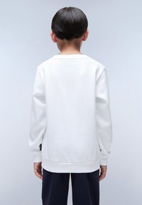 Sudadera blanca de manga larga, textura suave, cuello redondo y puños acanalados. Presenta una etiqueta en el lateral cerca del dobladillo.
