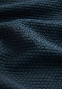 Tejido oscuro azul marino texturizado con un patrón de cuadrícula, que presenta pequeños diamantes en relieve, creando una superficie suave pero táctil.