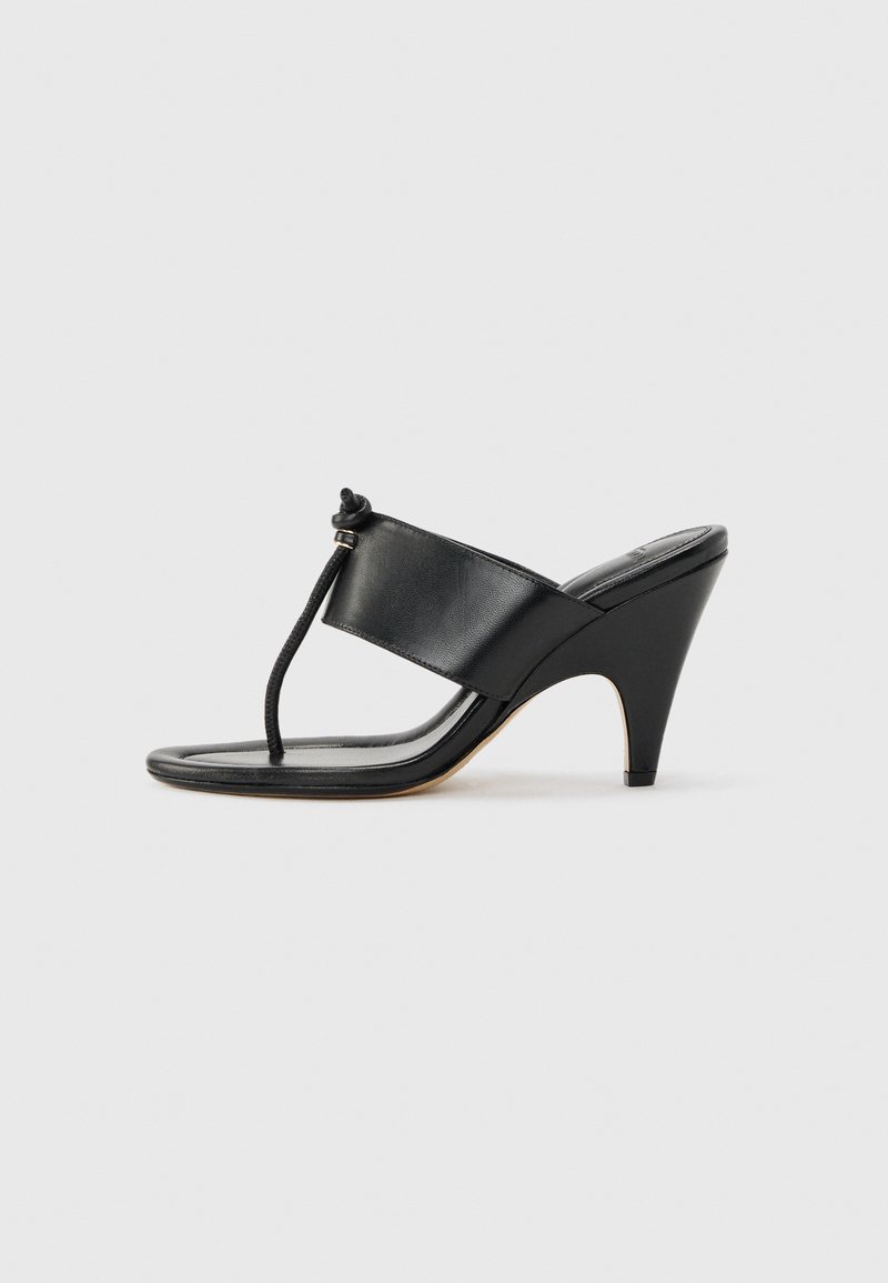 Μαύρο σανδάλι με ψηλό τακούνι, με φαρδιά μπροστινή λουρίδα και δακτύλιο για τα δάχτυλα που διαθέτει λεπτομέρεια με κόμπο από κορδόνι, εμφανίζεται σε πλευρικό προφίλ σε λευκό φόντο.