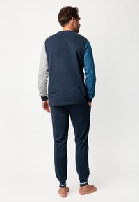 Conjunto de ropa de estar por casa de algodón que incluye una parte superior azul marino con mangas gris y azul, y pantalones a juego con puños a rayas, diseñado para la comodidad.