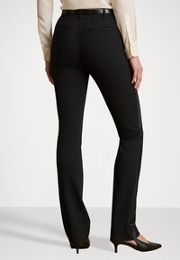 Čierne elegantné nohavice s hladkou textúrou, so slim fit strihom a zadnými vreckami, skombinované s špicatými čiernymi lodičkami.