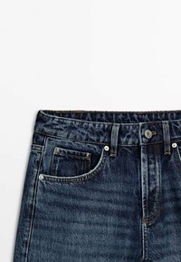 Dunkelblaue Jeans aus Denim mit hoher Taille, Fünf-Taschen-Design und Metallbeschlägen am Verschluss und den Taschen. Texturiert mit leichtem Glanz.