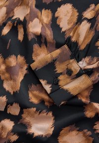 Tissu noir avec de grandes taches irrégulières marron et beige imprimé léopard et un poignet avec deux boutons noirs.