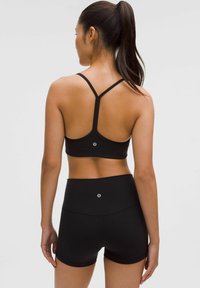 Fekete sportos crop top, racerback dizájnnal, magas derekú fekete rövidnadrággal párosítva. Az anyag sima, enyhe fényével.