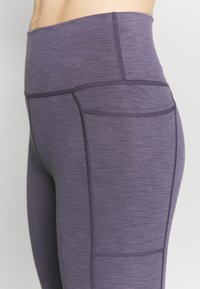 Fioletowe legginsy o wysokim stanie wykonane z teksturowanej tkaniny, z pionowymi szwami i bocznymi kieszeniami dla dodatkowej funkcjonalności.