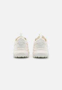 White athletic shoes featuring a mesh upper, thick rubber sole, rear pull tab, and minimal detailing, designed for comfort and support.