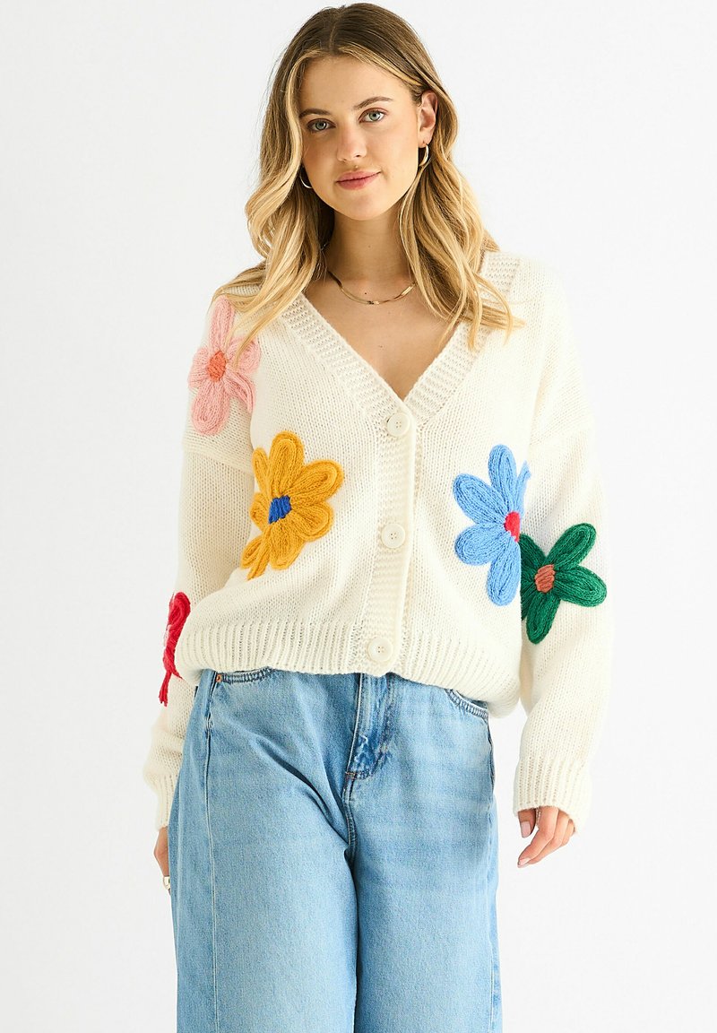White knitted cardigan featuring colorful embroidered flowers in pink, yellow, blue, and green. Button front and V-neck design.