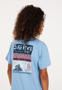 Modrá bavlněná trička s odvážnými potisky na zádech: logo "Surf Fever", vlny a abstraktní obrázky v různých barvách.