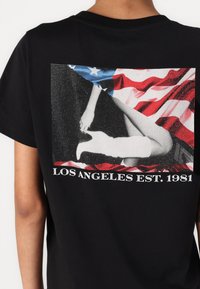 Black cotton t-shirt with a large graphic on the back featuring a person against a red and white abstract background, with "LOS ANGELES EST. 1981" text.