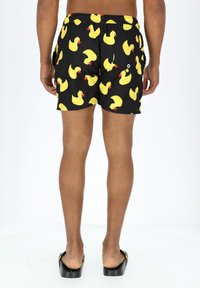 Zwarte zwemshorts met een patroon van gele rubberen eendjes. Elastische tailleband met aantrektouw, zakken aan de zijkanten en een gladde structuur.