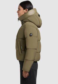 Olive green puffer jacket with a high collar and hood, featuring a branded patch on the arm, zipped side pockets, and a quilted design.