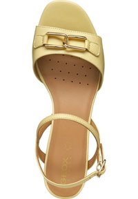 Sandalias de tacón alto de cuero amarillo con una correa regulable en el tobillo, banda frontal ancha y acentos en tono dorado. Plantilla texturizada con perforaciones.