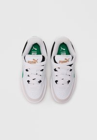 Et par hvite Puma-sneakers med grønne detaljer og gull Puma-logo på tungen, sett ovenfra på en hvit bakgrunn.