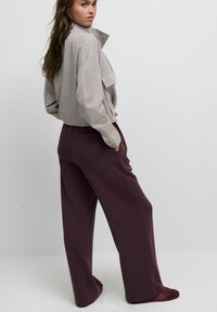 Cămașă gri deschis cu nasturi și guler, asortată cu pantaloni largi bordo și balerini roșii, prezentând texturi moi și un croi lejer.