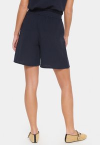 Marineblaue Shorts aus strukturiertem Stoff, mit einem lockeren Schnitt und einem elastischen Bund. Der Saum ist gerade und endet oberhalb des Knies.