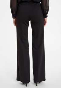 Zwarte wijde pantalons van een gladde stof, met subtiele glitters en een hoge taille, gecombineerd met een sheer zwart blouse.