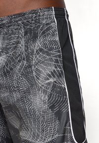 Sorte træningsshorts med et gråt abstrakt mønster, der har hvid piping langs sømmene og et åndbart meshpanel i siderne.