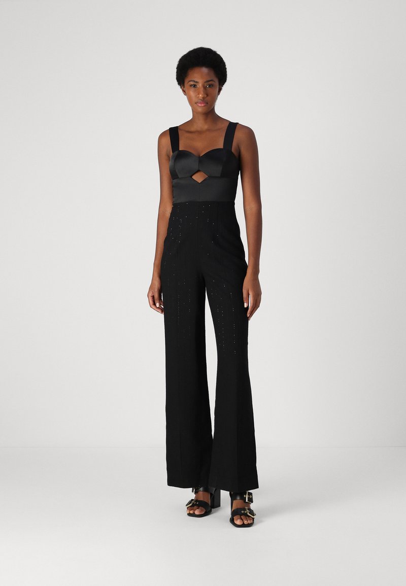 Svart jumpsuit med en satinöverdel och nyckelhålsutskärning, vida byxor och diskreta utsmyckningar. Strappy svarta klackar fulländar looken.