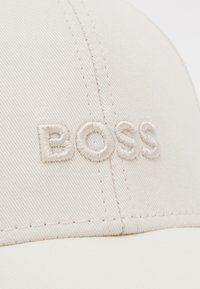 Cappellino da baseball beige chiaro in cotone con logo "BOSS" ricamato in filo coordinato. Caratterizzato da visiera curvata e tessuto testurizzato.
