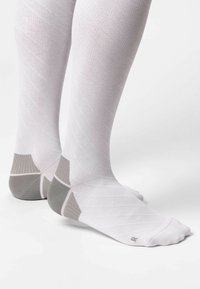 Calze compressive bianche con motivo diagonale, rinforzo grigio sul tallone e sulla punta, texture liscia e supporto arco a coste.