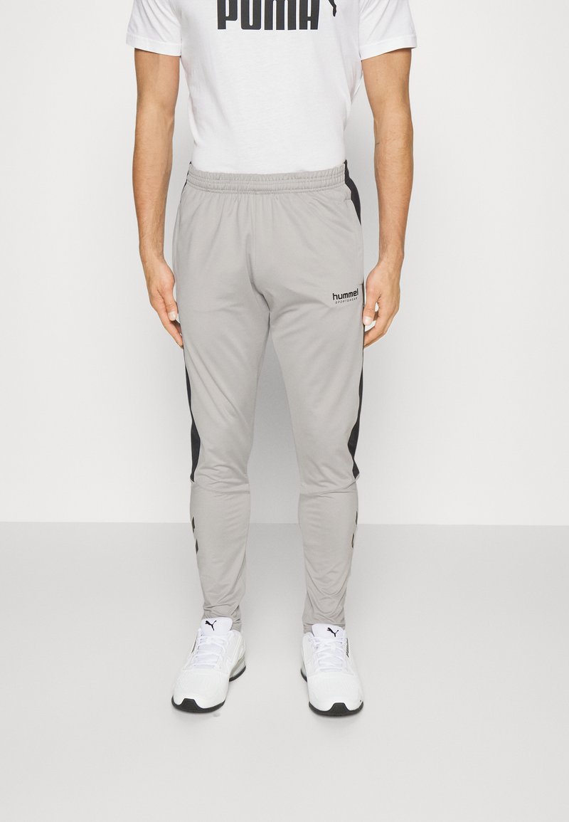 Grå sportbyxor med svarta sidostråk, elastisk midja och slim fit. I kombination med vita sportskor. Diskret logotyp synlig.